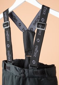 Pantalon en tissu noir avec bretelles grises ajustables portant la marque "ZIGZAG", boutons noirs, ceinture élastique et fermeture velcro.