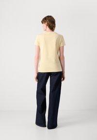 T-shirt giallo chiaro a maniche corte realizzato in morbido tessuto, abbinato a jeans a gamba larga blu scuro, visto da dietro.