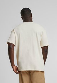 Crèmekleurig katoenen T-shirt met korte mouwen, ontspannen pasvorm en een ronde halslijn. Effen achterkant zonder zichtbare patronen of hardware.