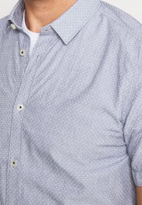 Světle modrá košile na knoflíky s texturovaným vzorem, krátkými rukávy a rozšířeným límcem. Obsahuje bílé knoflíky a pohodlný střih.