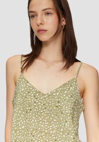 Groene mouwloze top met een V-halslijn, voorzien van een stippenpatroon in het wit. De stof lijkt textuur te hebben met dunne verstelbare bandjes.