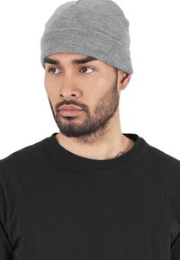 Grå ribbestrikket lue laget av strikket stoff. Har en tett passform og enkelt design. Bæres med en svart crewneck-skjorte.