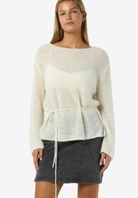 Maglione lavorato a maglia color crema con una vestibilità ampia, dotato di coulisse in vita, texture a coste e maniche larghe, abbinato a una gonna in denim scuro.