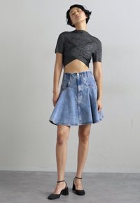 Pelēks krustveida cropped tops, apvienots ar gaiši zilu denim A līnijas svārku, kuram ir pogu aizdare un apakšmalas apdare. Melni blokveida papēži.