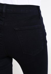 Mörk tvättade denimjeans med en figurnära design, som har bakfickor och en slät, lätt texturerad yta.