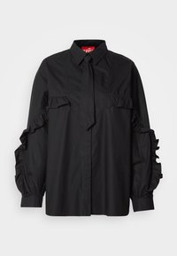 Blouse noire à manches longues avec col et cravate étroite assortie, présentant des détails froncés sur les manches et la poitrine.