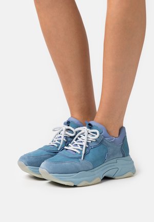 Modrá teniska s kombinací semišových a hladkých materiálů, vybavená bílými tkaničkami, robustní podrážkou a kontrastními světle modrými akcenty.