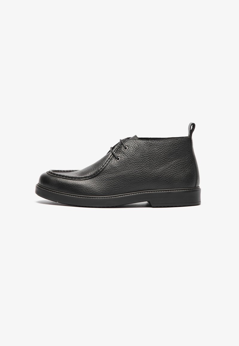 Botas de tobillo de cuero negro con acabado texturizado, punta redonda, diseño de cordones y suela de goma baja. Cuenta con un pequeño tacón y una lengüeta.