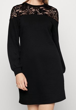 Schwarzes Kleid mit einem Spitzenbesatz an den Schultern, langen Ärmeln, Rundhalsausschnitt und lockerer Passform. Glatte Textur und mittellange bis zur Oberschenkelmitte.