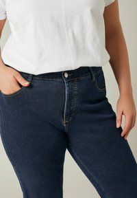 Jeans in denim blu scuro caratterizzati da un design aderente con vita alta, stile a cinque tasche e cuciture dorate a contrasto sui bordi.