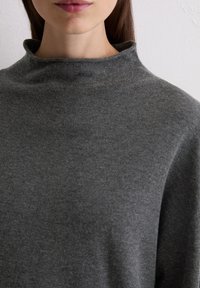 Pull à col roulé gris avec une texture douce et lisse, et une coupe légèrement décontractée, doté d'un col haut qui se plie doucement.