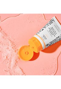 Gel cleanser tube with a white body and black graphic design; orange cap and pump; positioned on pink surface with bubbly texture.