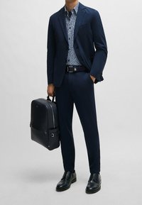 Námořnický oblek s košilí s vzorem, na které jsou bílé tvary, doplněný černým koženým batohem a leštěnými  černými botami.