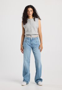 Grey sleeveless knit top with front buttons, paired with light blue flared jeans. White sneakers complete the outfit. Smooth fabric, casual style.