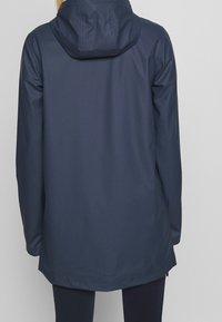 Navy vattentät jacka med huva, mjuk textur, långa ärmar och rak passform, med en dragkedja och sidofickor. Bakvy visas.