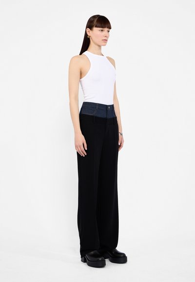 Black wide-leg pants with a denim-accented waistband. Model wears a white sleeveless top and chunky black platform shoes.