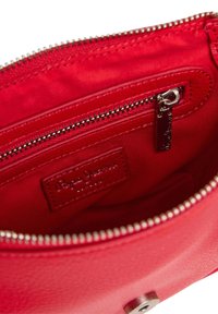 Interno di una borsa a tracolla in pelle rossa, con una tasca con zip, texture liscia e un'etichetta in pelle con marchio, arricchita da dettagli in metallo argentato.