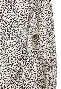 Blusa de manga curta em creme com estampa de leopardo preta, apresentando detalhes de franzido e botões transparentes ao longo do lado para fecho.