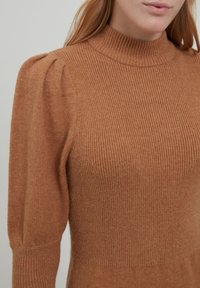 Maglione a collo alto a coste color ruggine, con dettagli strutturati sulle spalle e una trama morbida, dotato di maniche lunghe aderenti.