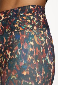 Legginsy o wysokim stanie z kolorowym abstrakcyjnym wzorem w odcieniach niebieskiego, pomarańczowego i kremowego; na pasie znajduje się czarne logo "STRONGER".
