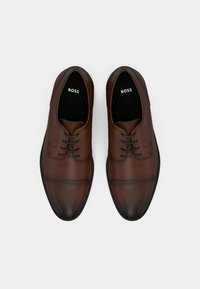 Barna bőrből készült, fűzős cipők sima felülettel, díszítő perforációkkal és lekerekített orral. Belsejében „BOSS” felirattal.
