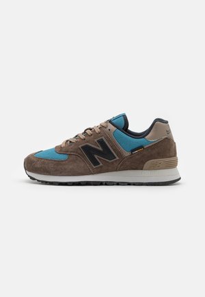 Baskets New Balance marron et bleu avec des détails en daim, logo noir et semelle blanche, vues de côté sur fond blanc.