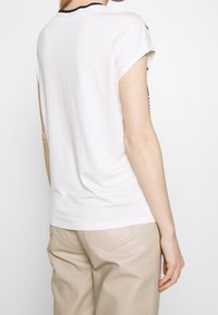White short-sleeve t-shirt with a round neck and black trim, paired with light beige pants. Smooth fabric with a relaxed fit and a subtle design.