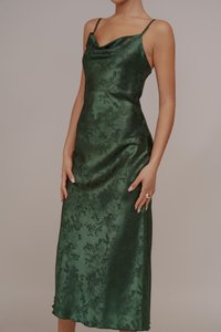 Πράσινο σατέν φόρεμα με ντεκολτέ σε σχήμα καμπάνας, λεπτές τιράντες και λουλουδάτο σχέδιο. Το ύφασμα έχει λεία, γυαλιστερή υφή και εφαρμοστό σχήμα.