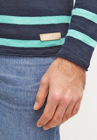 Laivastonsininen pitkähihainen paita, jossa vaaleanturkoosit raidat, resorit hihansuissa ja nahkainen etiketti. Yhdistetty vaaleansinisiin farkkuihin.