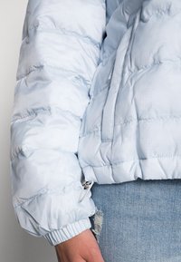 Világoskék puffkabát steppelt textúrával, rugalmas mandzsettákkal és oldalsó zsebbel. Simma, fényes felülettel és puha anyaggal rendelkezik.