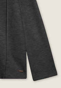 Maglietta grigia a maniche lunghe con texture a coste, dotata di un'etichetta sul fondo discreta. Il tessuto sembra morbido e leggermente elasticizzato.