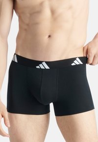 Svarta boxershorts i mjukt tyg, med ett brett elastiskt midjeband som har en vit Adidas-logotyp och subtila sömnadsdetaljer.