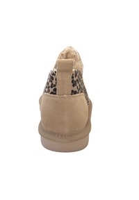 Bottines beige avec un panneau en tissu doux présentant un imprimé léopard noir. La semelle est en caoutchouc beige et il y a une petite languette au dos.