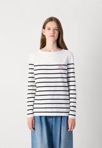 Langsleeve gestreept shirt in wit en marineblauw, met een ronde halslijn en een klein rood logo op de borst. Zacht katoenen materiaal.