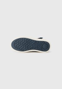 Marineblå sneakersåle med teksturert gummi, bølgete mønster og sirkulære detaljer. Kremfarget mellomsåle for kontrast og støtte.