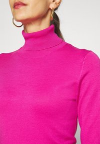 Fuchsia turtleneck sweater in a smooth knit fabric with long sleeves and ribbed accents at the cuffs and collar.