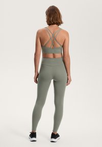 Athletic wear set in muted green, featuring a cropped top with crisscross straps and high-waisted leggings with a smooth texture and fitted shape.
