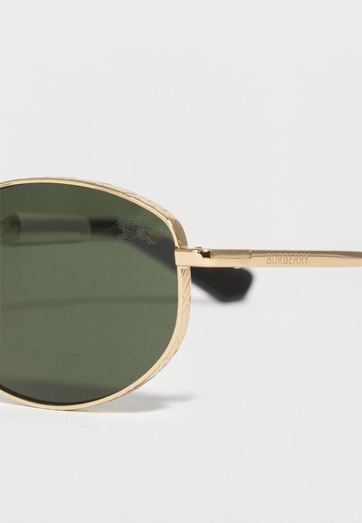 Γυαλιά ηλίου με χρυσό πλαίσιο, σκούρους πράσινους φακούς και χαραγμένο σχέδιο στο πλαίσιο, με λογότυπο Burberry χαραγμένο στον βραχίονα.