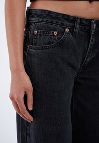 Black denim jeans with a high-waisted design, featuring copper rivets, five pockets, and a slightly faded texture.