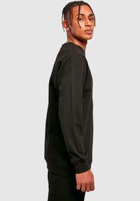 Black sweatshirt with long sleeves, ribbed cuffs, and relaxed fit. Smooth texture, crew neckline, and minimalist design.