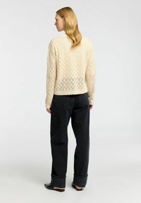 Maglione lavorato a maglia color crema con motivo a rombi, scollo a girocollo, polsini e orlo a costine. Abbinato a jeans scuri a vita alta e ballerine nere.