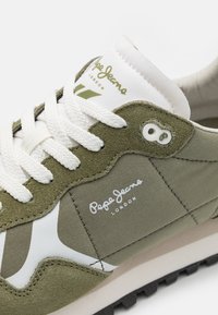 Zapatilla de ante verde y blanca con paneles texturizados, diseño de cordones, detalle de logo y suela de goma negra.