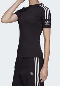 Svart tränings t-shirt med rund halsringning, korta ärmar och tre vita ränder på axlarna. Har en Adidas-logotyp på ärmen.