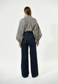 Gestreiftes, oversized Hemd in Creme und Marineblau mit Kragen, kombiniert mit dunkelblauen, hoch geschnittenen Schlagjeans mit kontrastierenden Nähten.