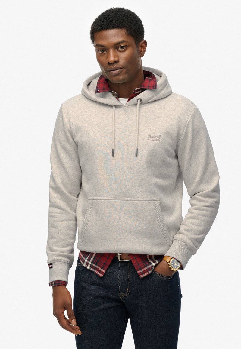 Lichtgrijze hoodie met een trekkoord en een voorzak, gedragen over een rood geruit shirt. Heeft een klein logo op de borst en een gestructureerde stof.