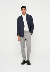 Ναυτικό διπλόκουμπο σακάκι, λευκό πουκάμισο, γκρι παντελόνι με άνετη γραμμή, μαύρα παπούτσια· λείο ύφασμα με αντιθετικά χρώματα και δομημένο σχέδιο.