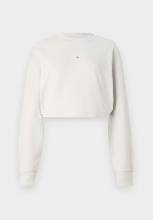 Zkrátená mikina zo svetlosivého materiálu, s dlhými rukávmi, klasickým výstrihom a malým logom v strede. Mäkká textúra.