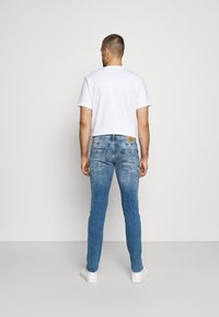 Slim-fit, vaaleansiniset farkut, joissa on kulutusjälkiä ja kaksi takataskua. Paritettu yksinkertaisen valkoisen t-paidan ja valkoisten tennareiden kanssa.