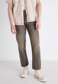 Beige, kortermet skjorte med teksturert overflate, kombinert med falmet, rette jeans og kremfargede høyhælte joggesko.