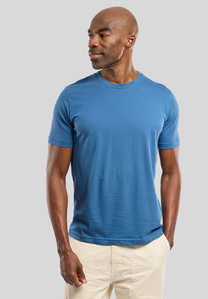 T-shirt bleu à manches courtes en tissu lisse avec un col rond, présentant une coupe décontractée et une texture subtile, associé à un short clair.